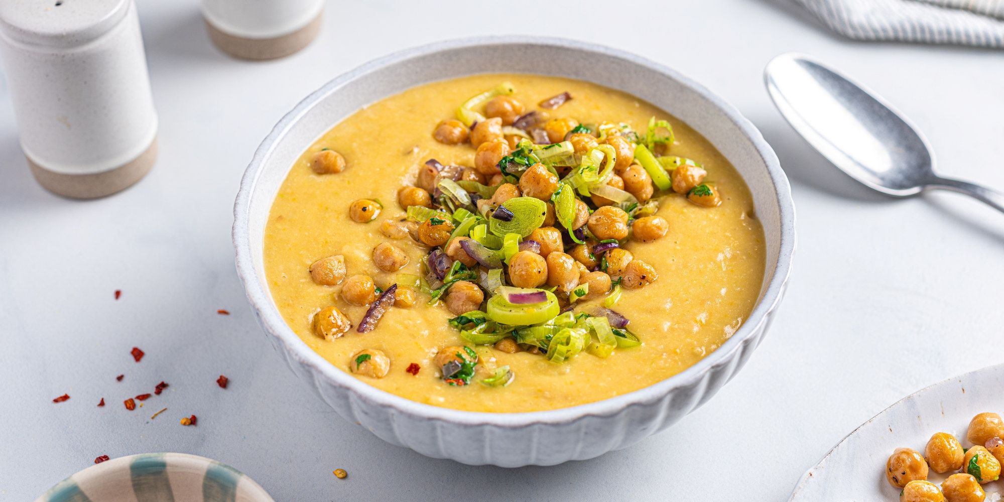 Kikerter og potetsuppe servert i en hvit bolle med garnityr av grønnsaker og krydder på toppen.