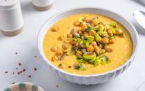 Kikerter og potetsuppe servert i en hvit bolle med garnityr av grønnsaker og krydder på toppen.