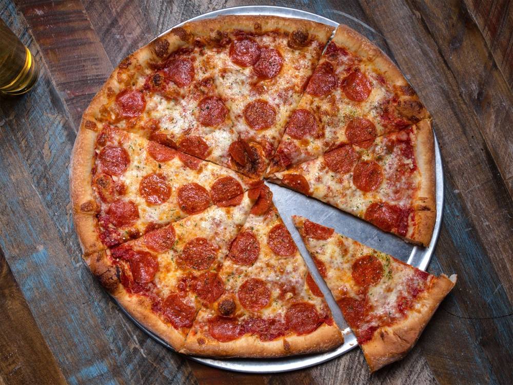 En pizza med pepperoni og ost på en treplate, med en pizzaskjærer som skjærer i den.