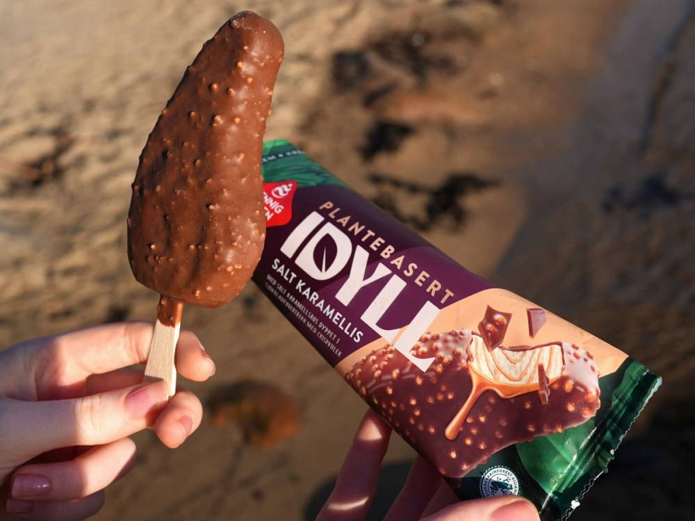 En person holder en sjokoladeis med sjokoladetrekk og en sjokoladebar med karamellsmak på stranden.