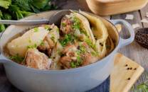 Fårikål i en gryte med hel kål, kjøtt og grønne urter, klar til servering.