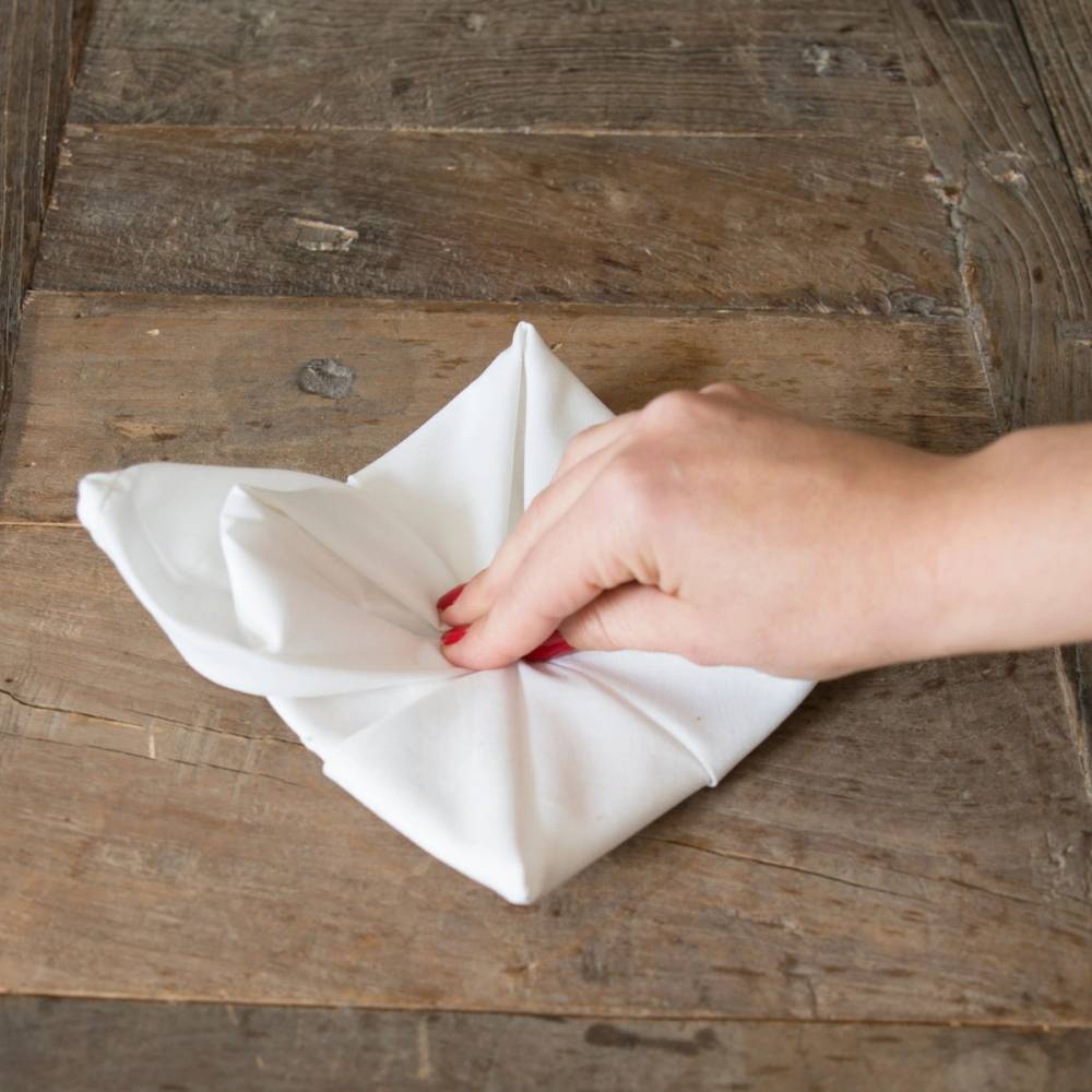 En hånd folder en hvit serviett på en treoverflate, klar til jul.