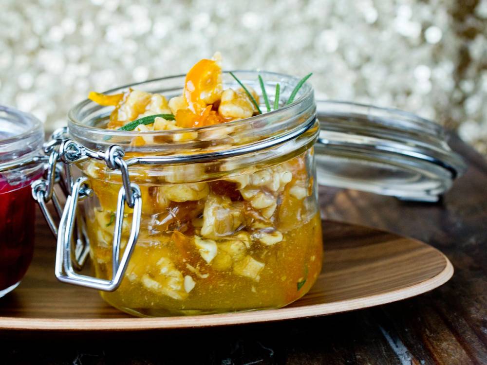 Honningstekte valnøtter i et glass med lokk, plassert på et rundt treplate