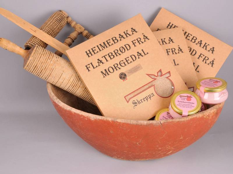 En keramisk bolle fylt med små pakker og en tresleiv, med et par papirposer med tekst om heimebakst og flatbrød fra Morgedal, samt små glass med rosa etiketter.
