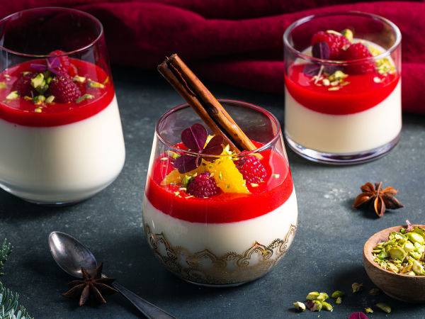 Tre porsjoner med panna cotta med jordbær og frukt på toppen, servert i små glass, med krydder og pynt rundt på en mørk overflate.