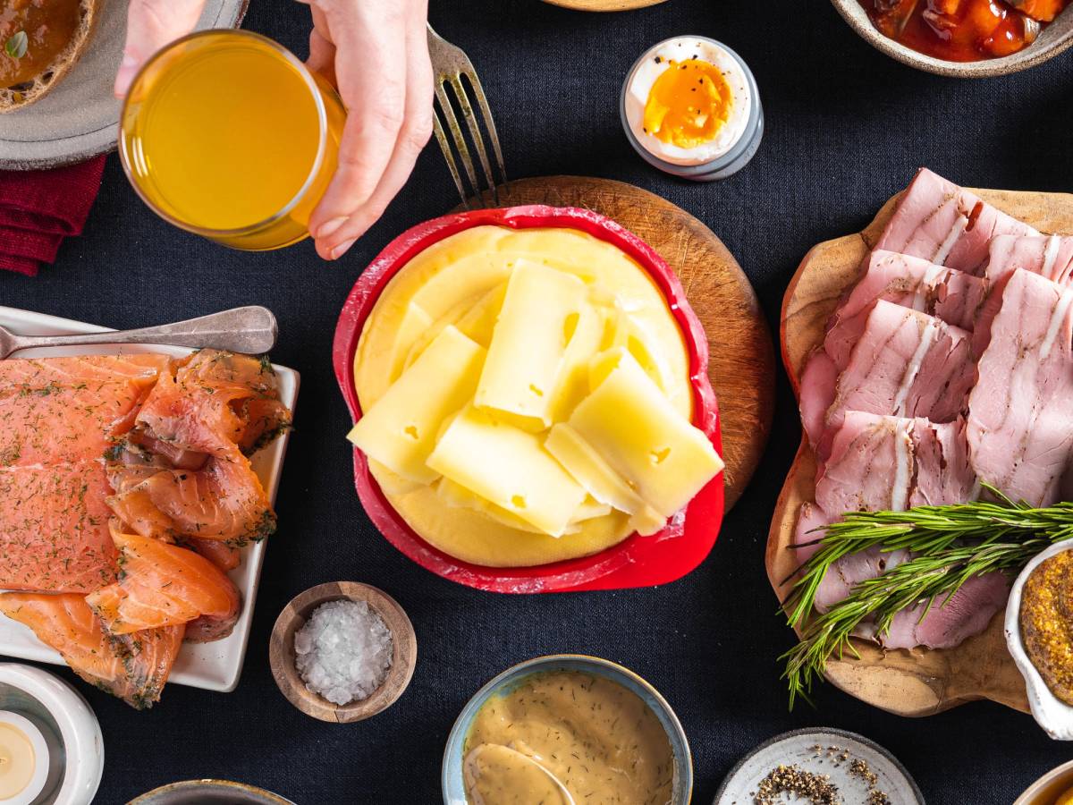 Julefrokostbord med ost, spekemat, egg, og ulike tilbehør på et mørkt bord.