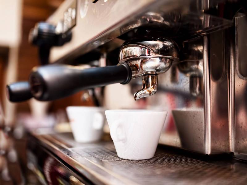 Kaffemaskin som lager espresso i en kaféinnstilling, med hvite kopper under dysene.