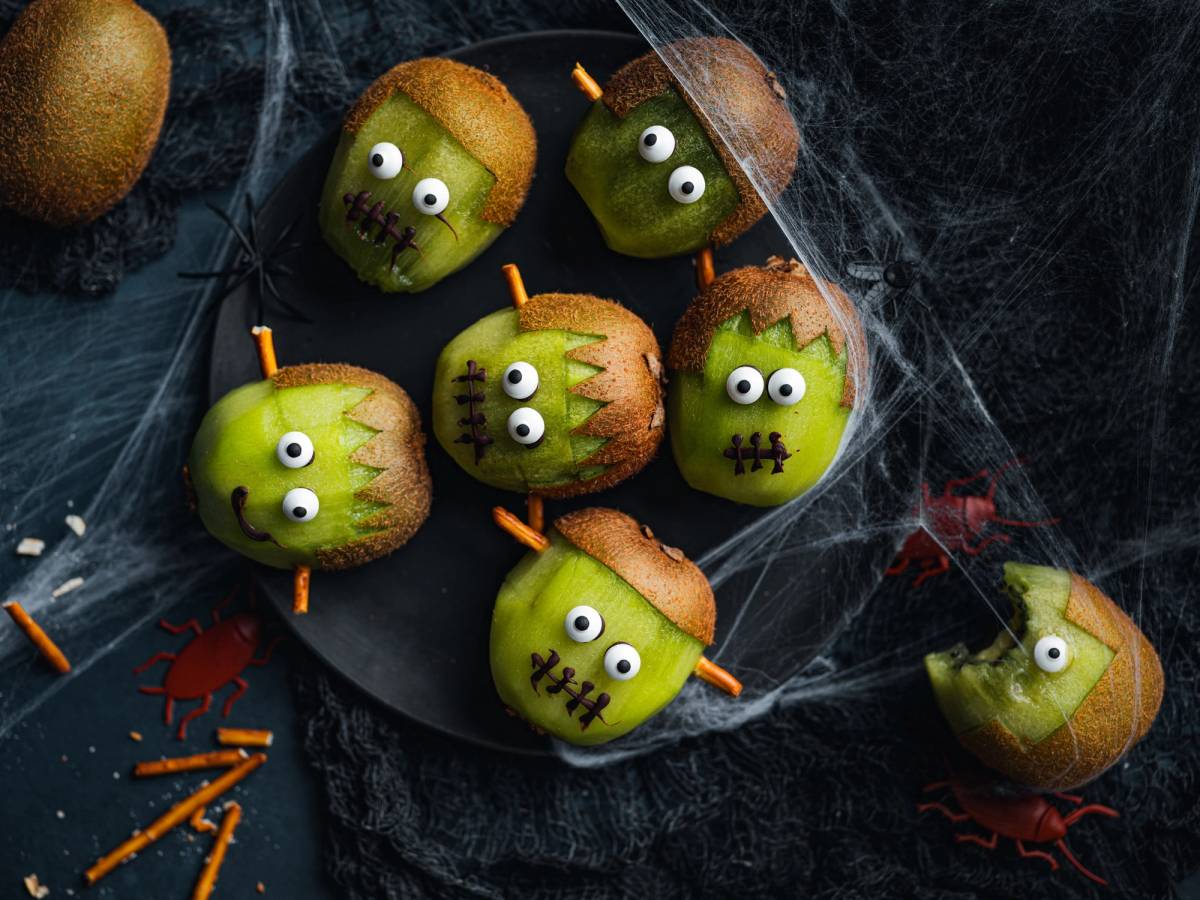 Eplepyntede snacks med ansikter og små horn, dekorert til Halloween, på en svart tallerken med spindelvev rundt.
