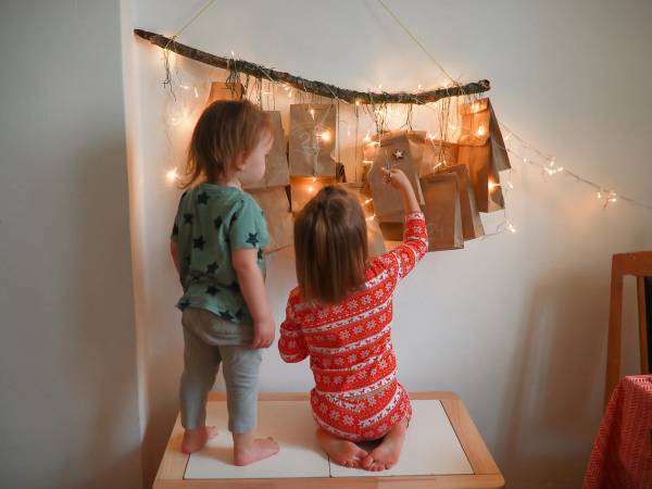 To barn lager en julekalender på en vegg med lys og dekorasjoner, en av barna peker mot kalenderen.