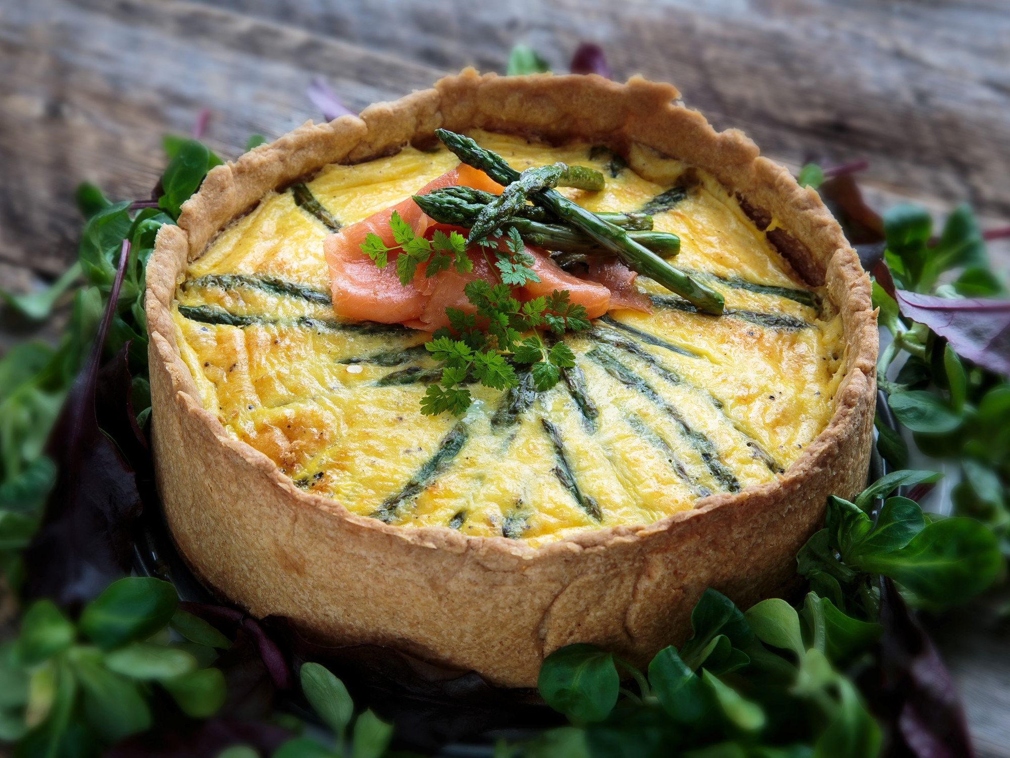 En pai med en gul eggerøre-fylling, pyntet med grønne urter og en liten skive laks, omgitt av grønne blader.