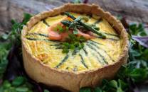 En pai med en gul eggerøre-fylling, pyntet med grønne urter og en liten skive laks, omgitt av grønne blader.