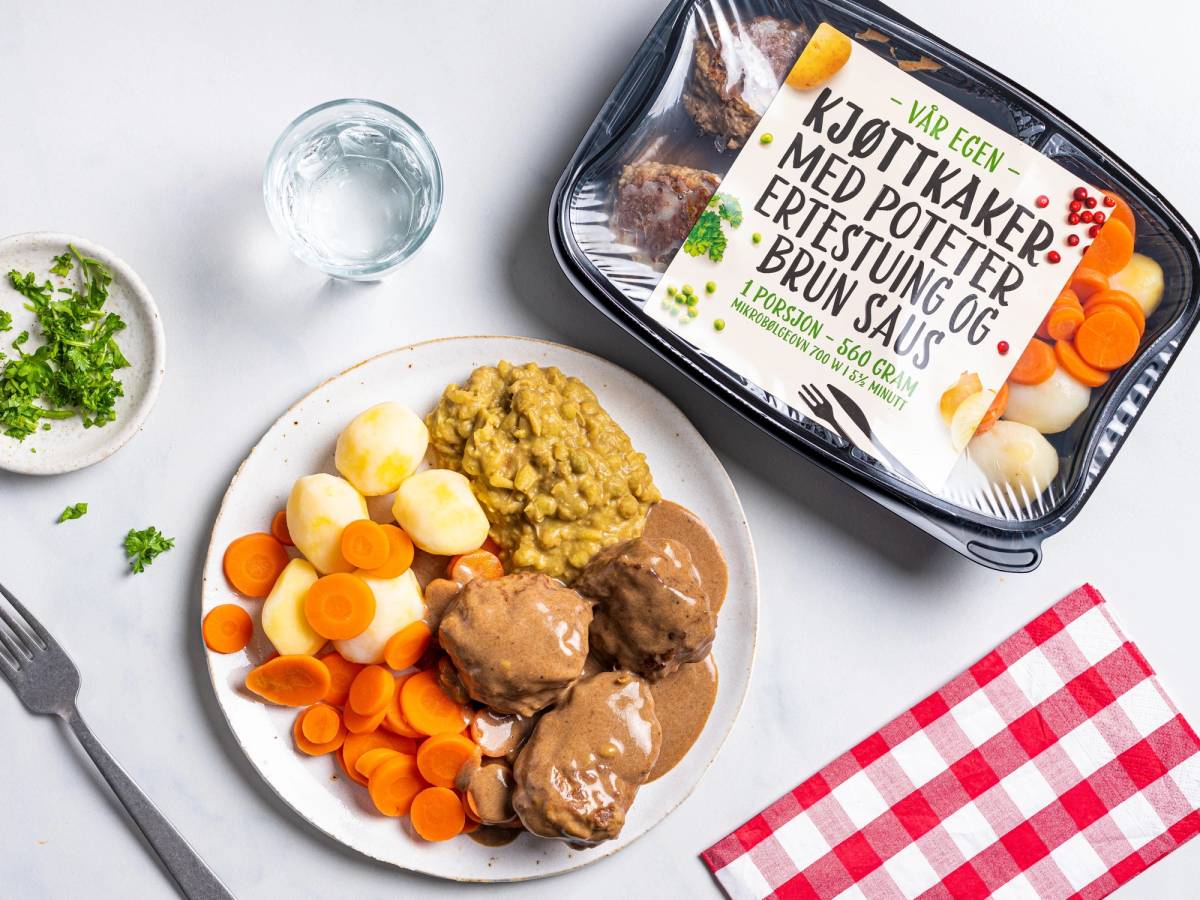 En porsjon kjøttkaker med poteter, gulrotstaver, erter og brunsaus på en hvit tallerken, med en pakke med kjøttkaker i bakgrunnen.