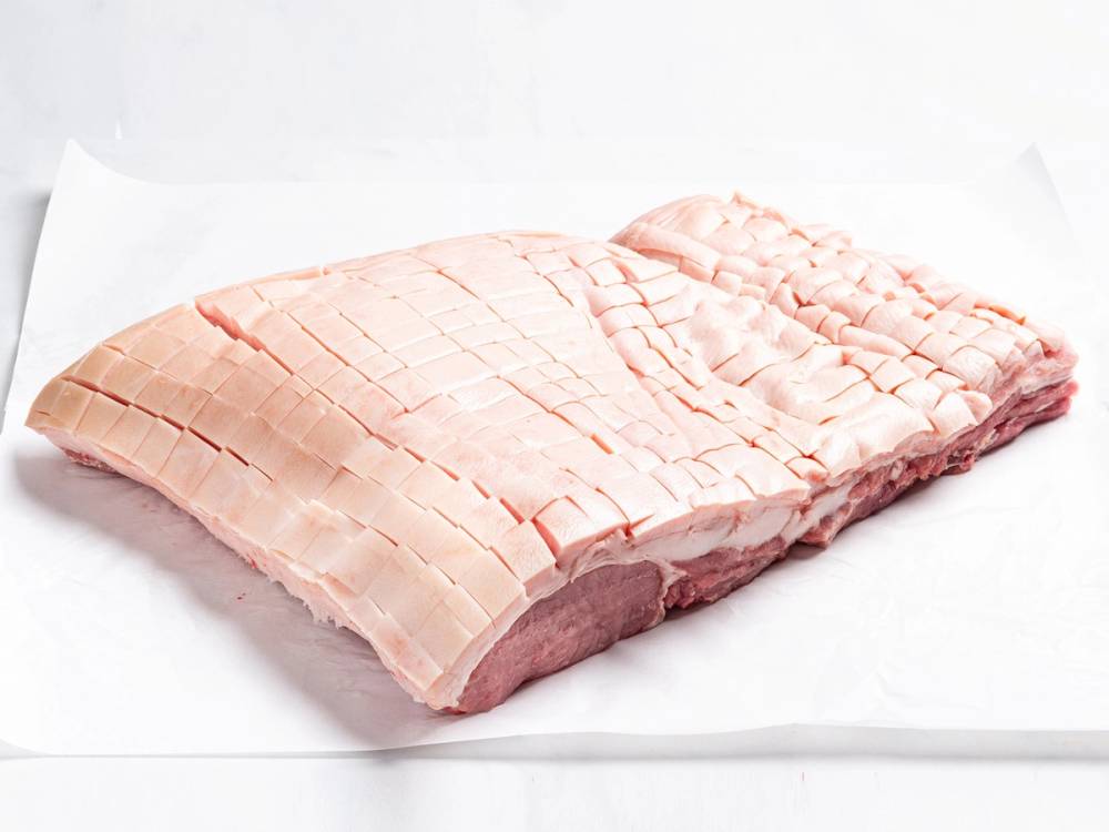 Rå juleribbe med snittflater, klar til å bli stekt eller ovnsbakt, liggende på hvitt underlag.