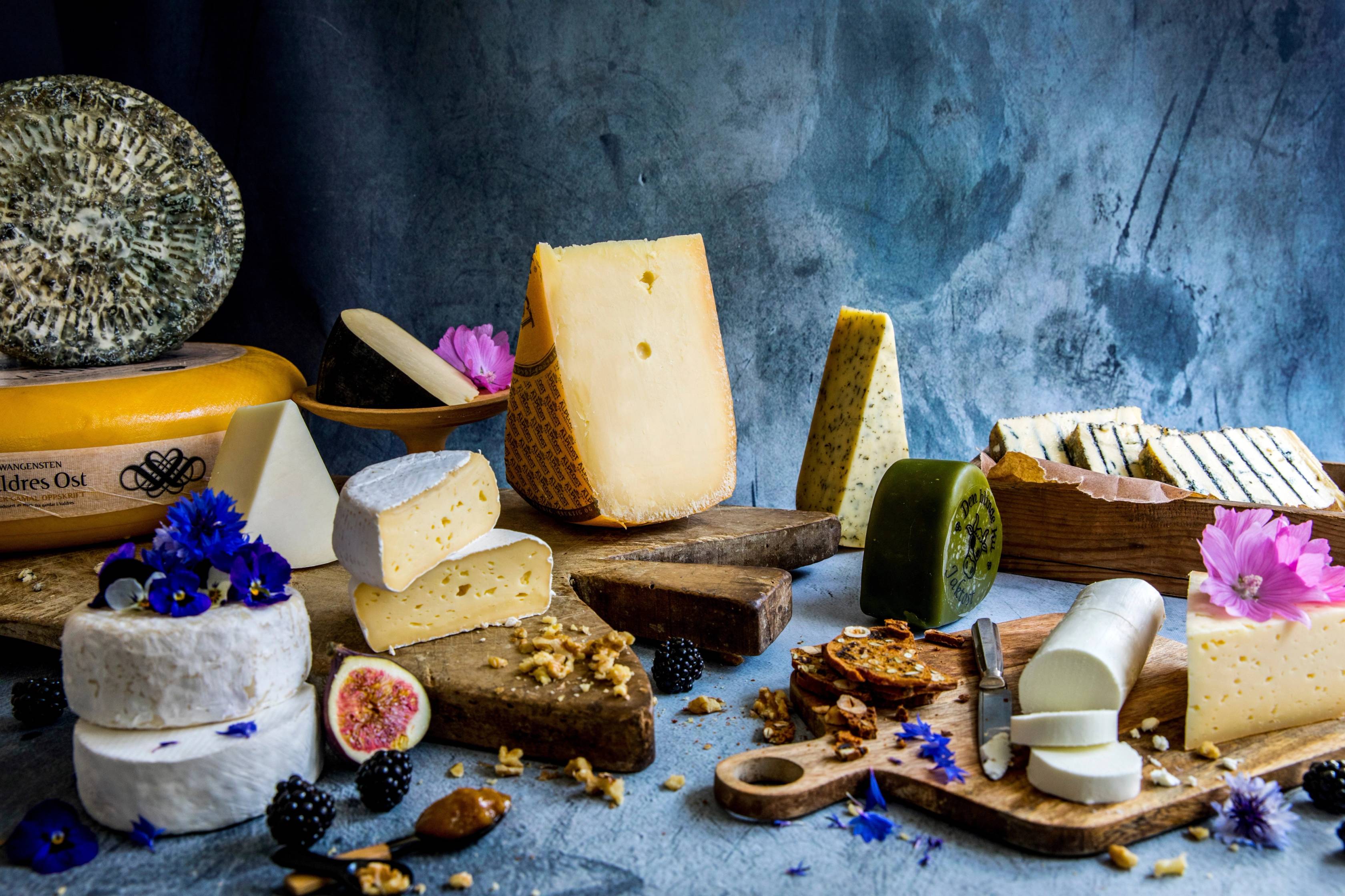 Et utvalg av ulike oster, nøtter og frukt på et bord med en blå bakgrunn.