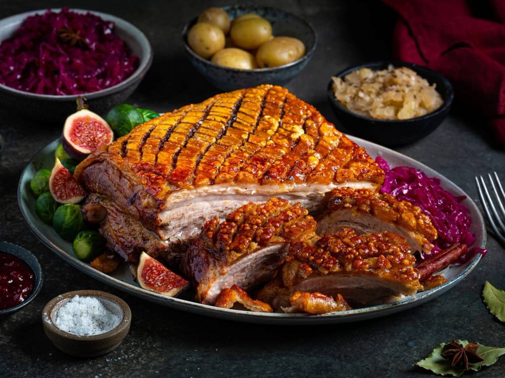 Ribbe med sprø svor, servert med surkål, poteter og tilbehør på et fat.