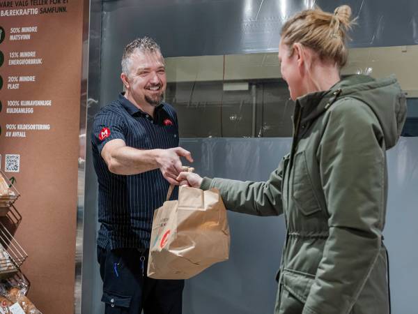 MENY-ansatt overleverer en Too Good To Go-pose til kunde.