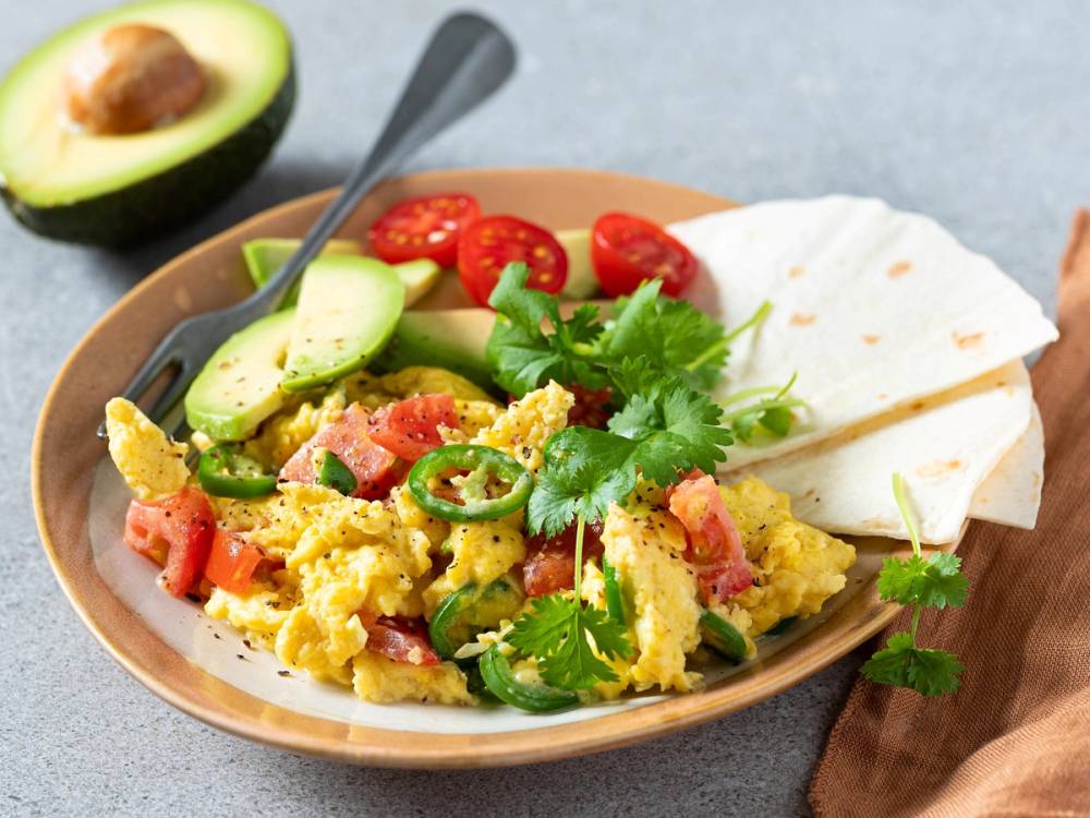 Meksikansk eggerøre med avokado, cherrytomater, tortilla og frisk koriander på en tallerken