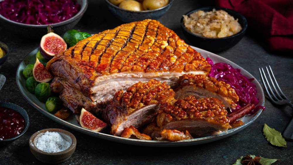 Ribbe med sprø svor, servert med tilbehør som rosenkål og julekrydder, på et festbord.