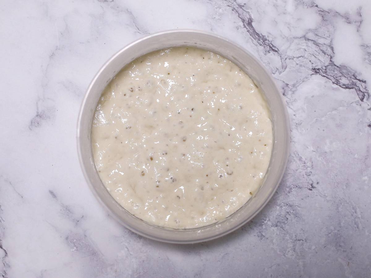 En bolle med hvit, jevnt blandet poolish-deig på en marmorgulvet.