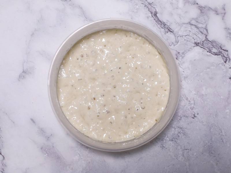 En bolle med hvit, jevnt blandet poolish-deig på en marmorgulvet.