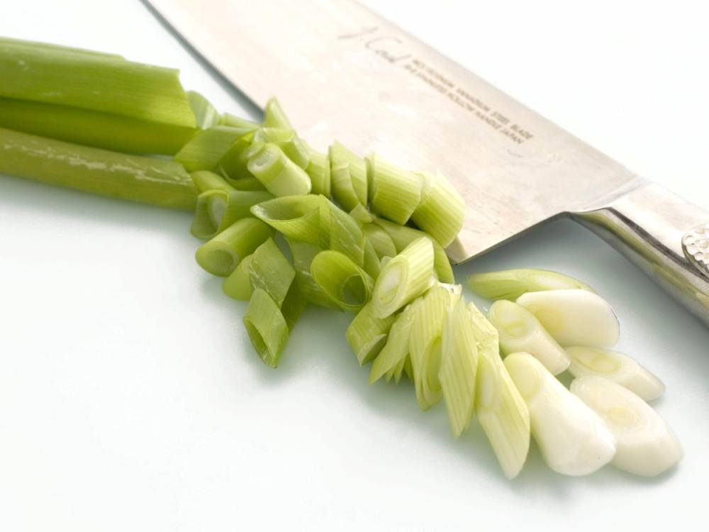 Varlok i skiver med grønne stilker og hvite blomster, liggende på et hvitt underlag.