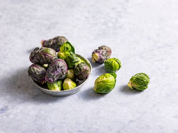 Rødkål og grønkål i en skål, med noen blader spredt rundt på en lys bakgrunn