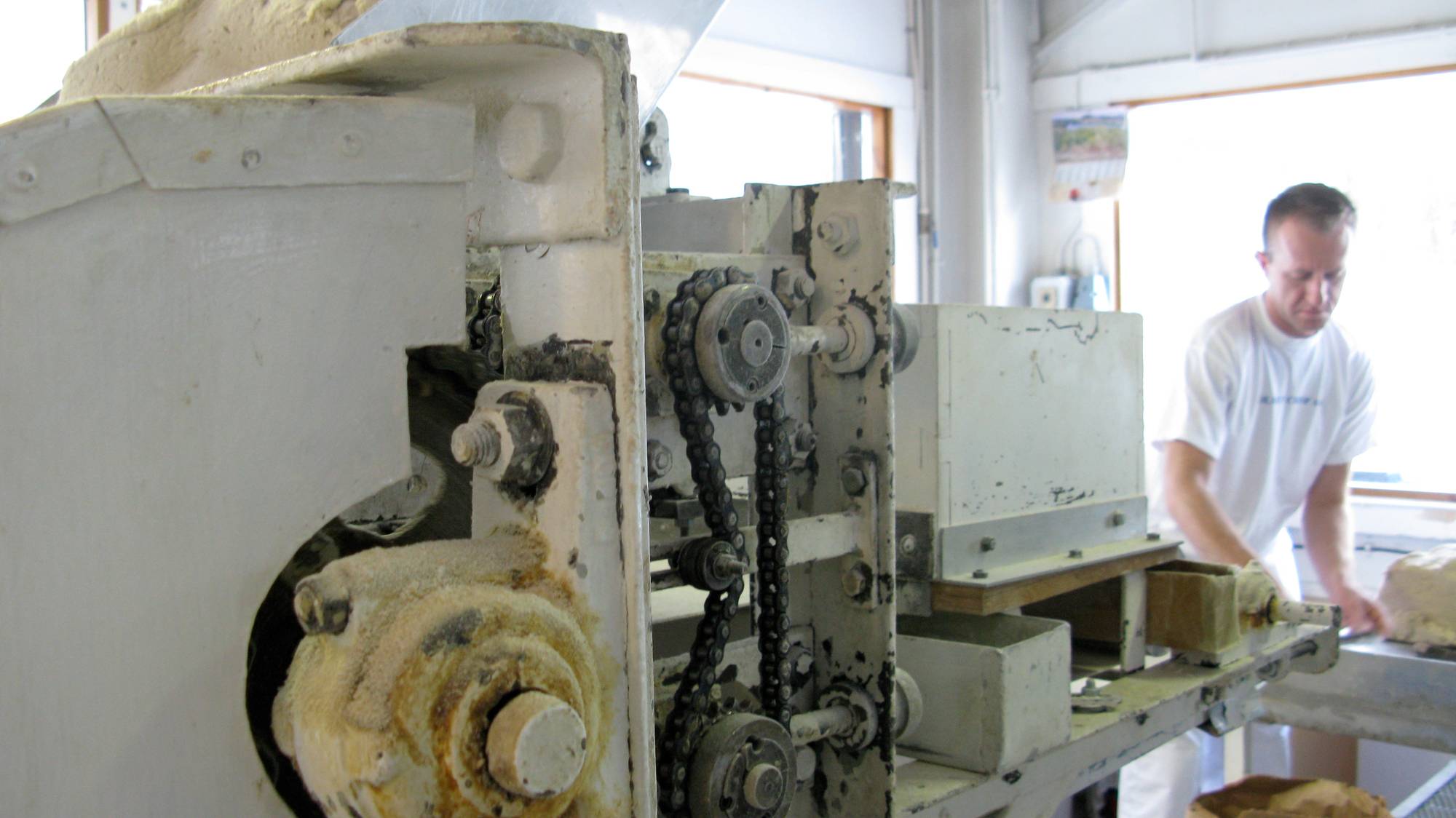 En person står ved en maskin i et industrielt verksted, med maskinen i fokus og personen i bakgrunnen.