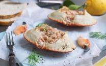 To krabbeskjell fylt med en kremet blanding, plassert på hvitt papir med dill og en gaffel ved siden av.