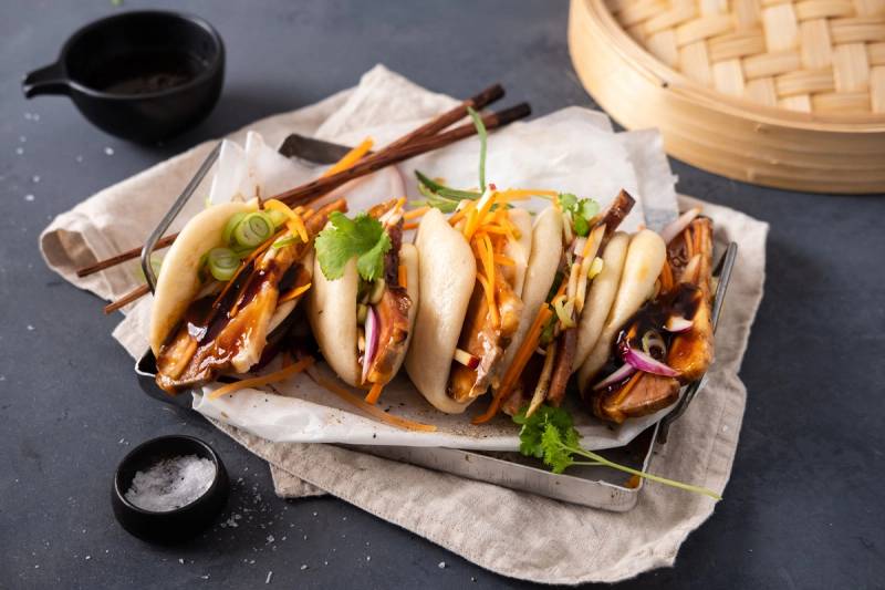 Steambuns fylt med kjøtt og grønnsaker, servert med soyasaus og frisk koriander på siden.