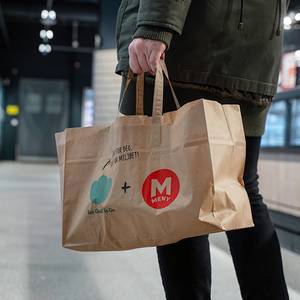 Person som holder en papirpose med To-good-to-go-logo i en butikk eller på et kjøpesenter.