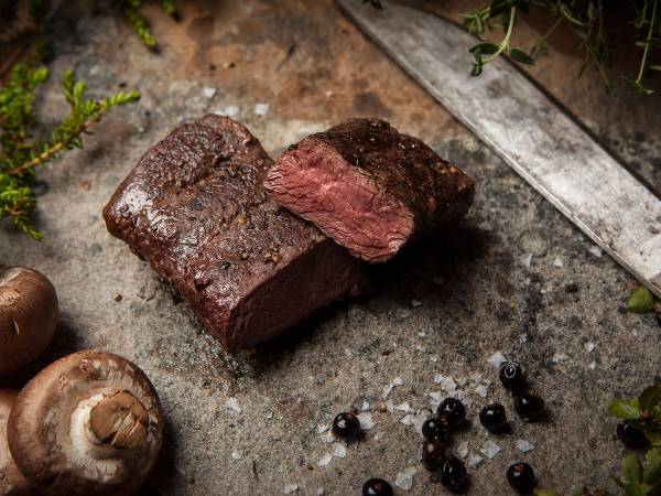 Kjøttstykker som er stekt på naturlige premisser, med sopp og svarte bær rundt på en stekeplate.