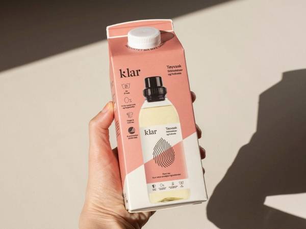 En hånd holder en kartong med drikke, der står 'Klar' på pakken, og det er en liten flaske inni kartongen.