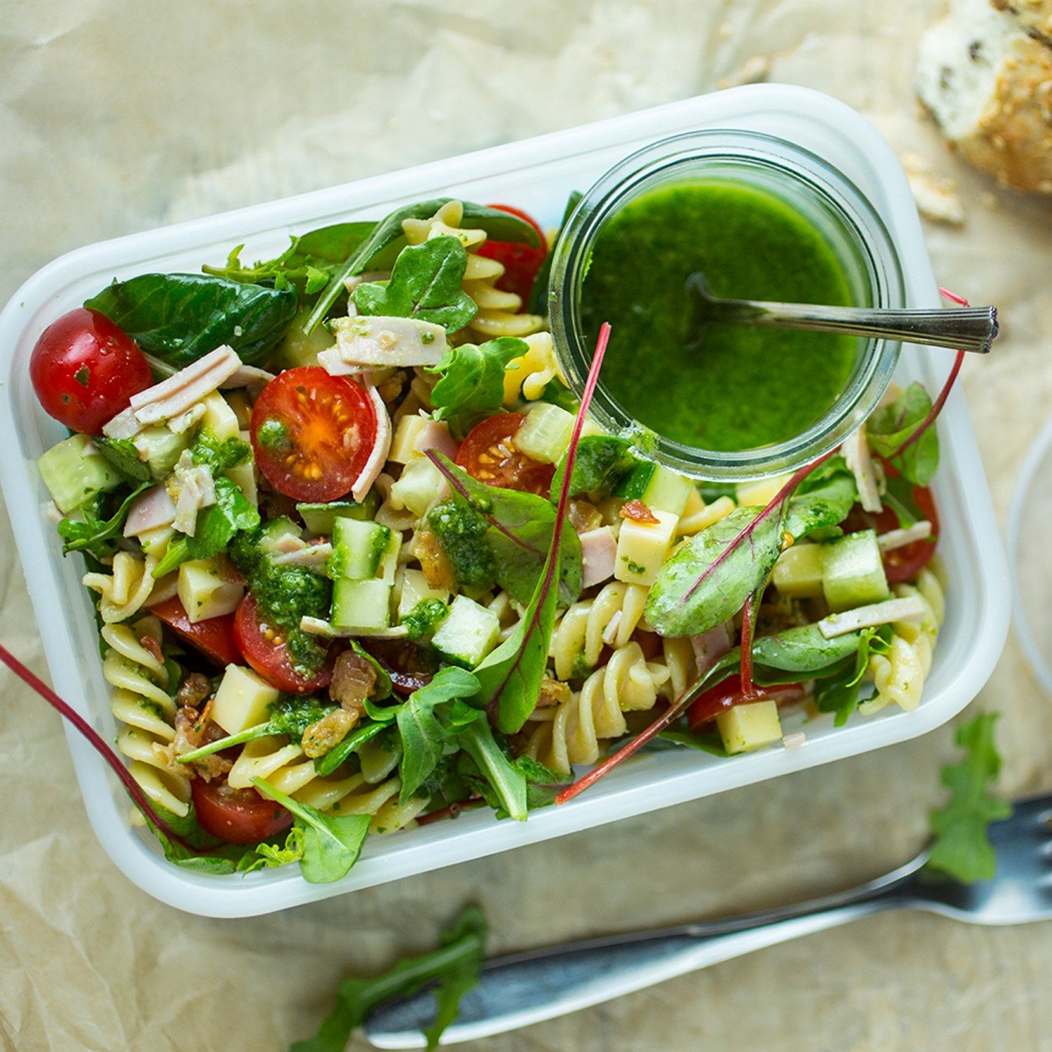 En salat med cherrytomater, agurk, salatblader og pasta, servert med en grønn dressing i en liten glasskrukke