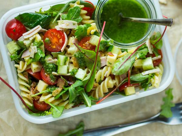 En salat med cherrytomater, agurk, salatblader og pasta, servert med en grønn dressing i en liten glasskrukke