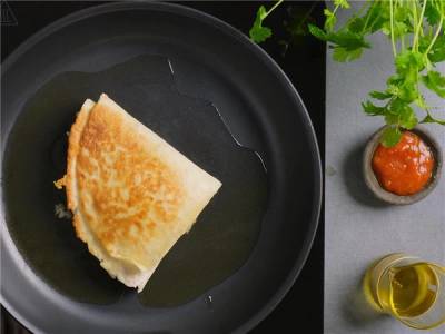 En stekt tortilla wrap i en svart stekepanne, med en liten plante med tomatsaus og en flaske med olje ved siden av.