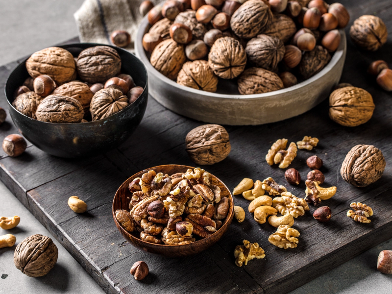 Nøtter i ulike boller og på et svart skjærebrett, med noen knuste nøtter foran.