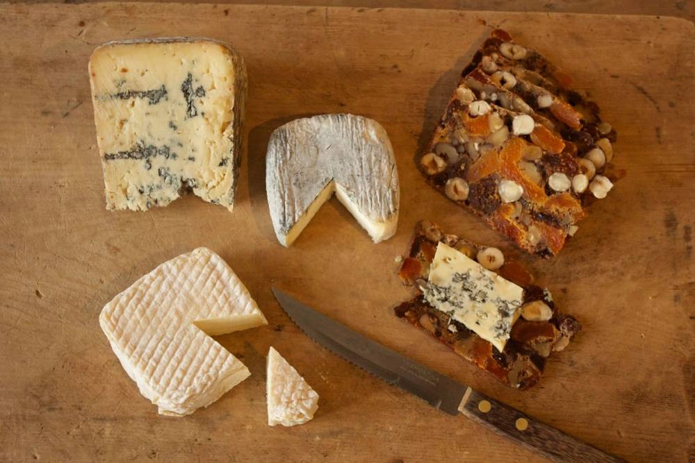 Ulike typer ost på et tre-etasjes ostefat med en kniv, plassert på et trebord.