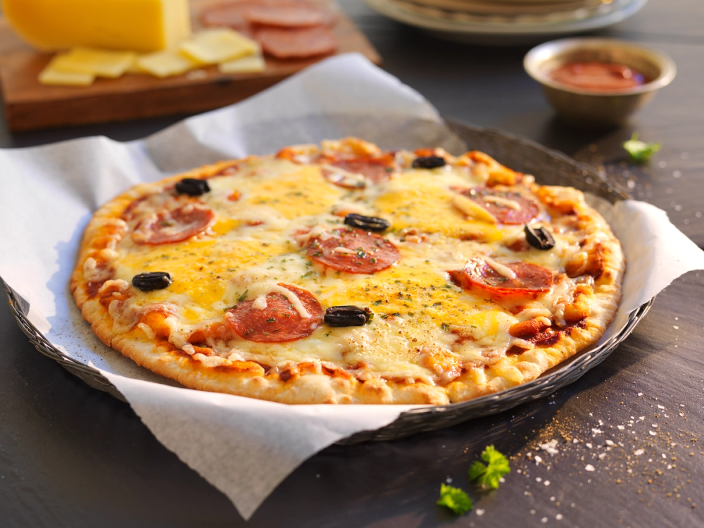 Pizza med chorizo, cheddarost og vellagret Valdresost, ser varm ut og ligger på et fat med et stykke ost og noen krydder ved siden av.