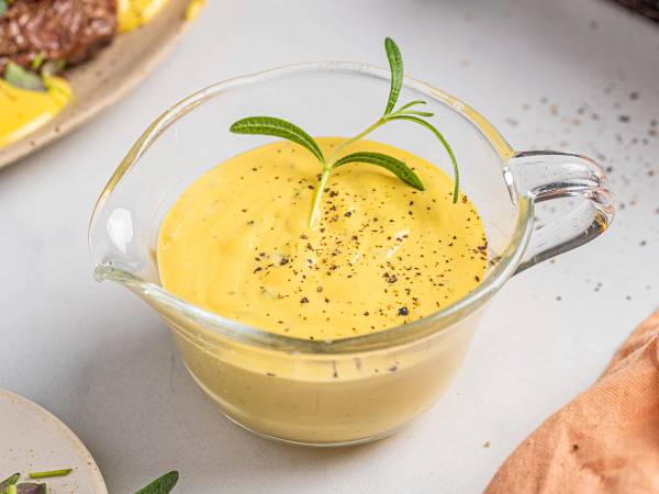 Kremet béarnaisesaus i en glasskål med urter og pepper på toppen