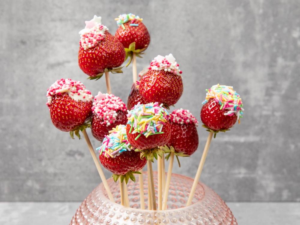Kakepyntede jordbær på pinne med fargerike strøssel og sukker på en kake, sannsynligvis til en babyshower.