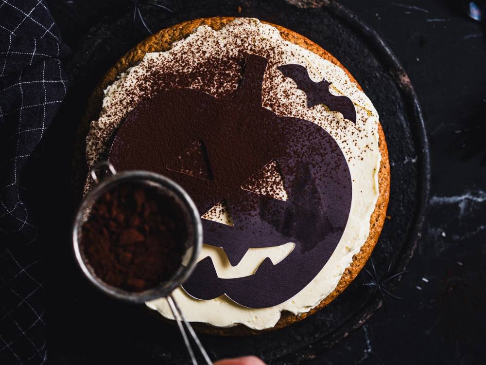 En Halloween-kake med pyntede gresskar- og flaggermusformer på toppen, sett fra oven.