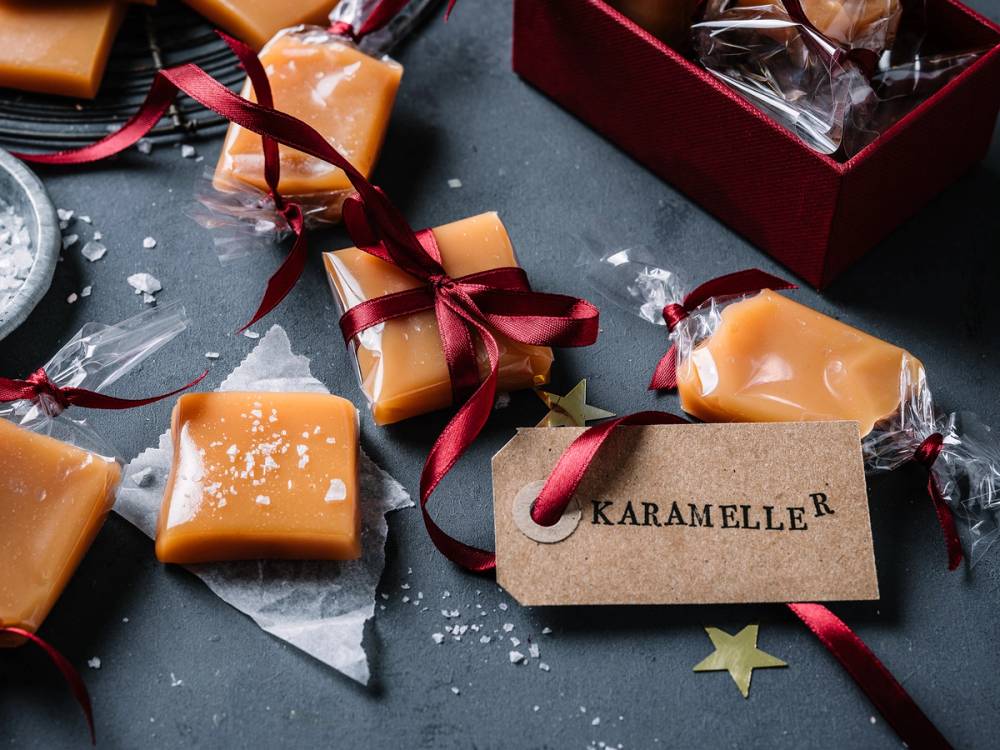 Små karamell- og godteposer med julestemning, pyntet med rød sløyfe og en tag med teksten 'Karameller'.