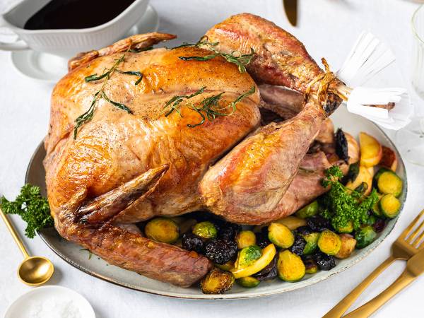 Stekt kalkun med sprøtt skinn, omgitt av ovnsstekte grønnsaker som poteter, brokkoli og gulrøtter, på et hvitt fat.