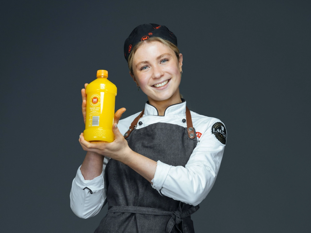 Person i kokkeantrekk holder frem en flaske ferskpresset juice med MENY logo