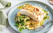 En tallerken med stekt kveitefilet toppet med skiver av mandler, servert med potetmos og grønnsaker, på et lyst bord.