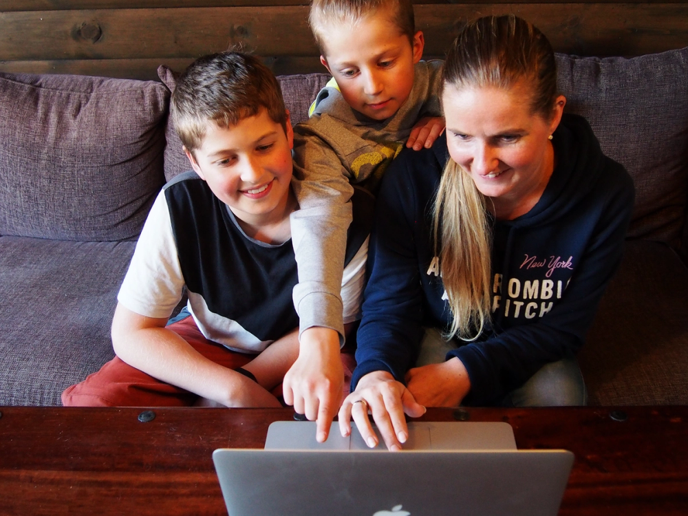 Tre barn sitter rundt et bord og ser på en bærbar datamaskin, med en sofa i bakgrunnen.