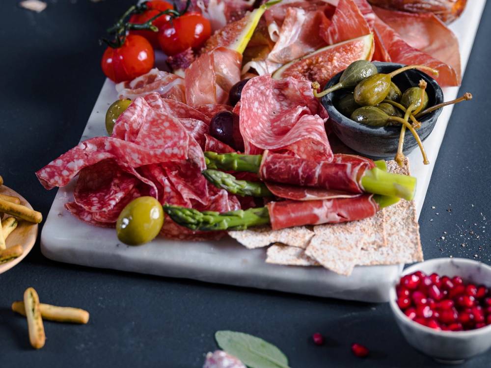 Et utvalg av spekemat, grønnsaker og småretter på et fat, klar for helgefeiring.