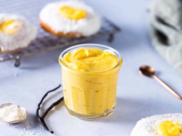 Vaniljekrem i et glass med noen småkaker rundt på et hvitt bord