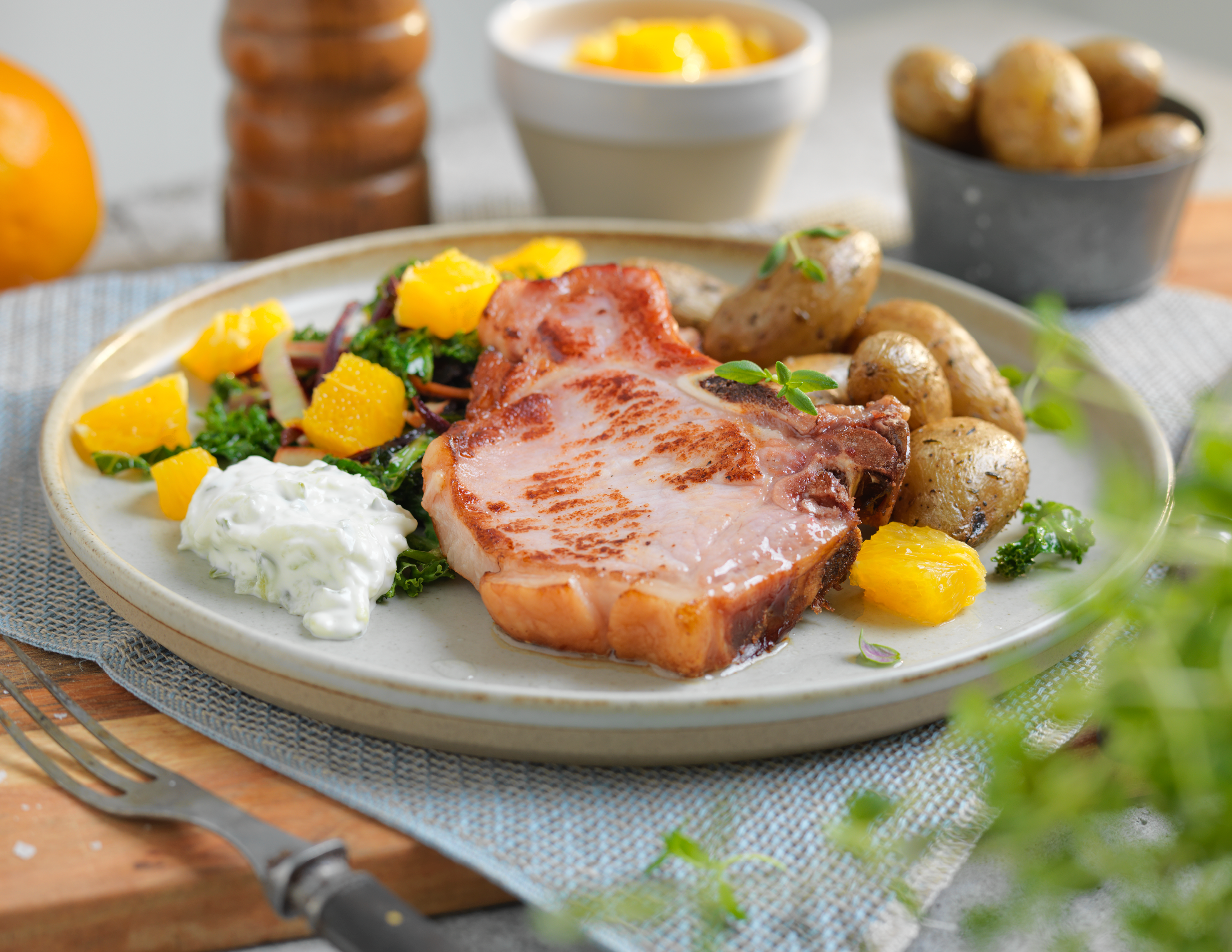 Sommerkoteletter med grønnkål, sopp og poteter på en tallerken, med en skål med smør og en annen med sopp i bakgrunnen.