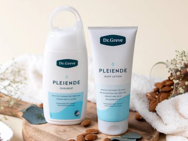 To pleiende produkter fra Dr. Greve, en flaske og en tube, plassert på et trebrett med nøtter og en hvit håndkle i bakgrunnen.
